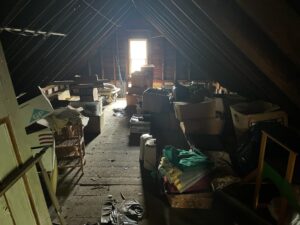 A full view of a house's attic. Several pieces of furniture, momentos and other various items litter the floor.