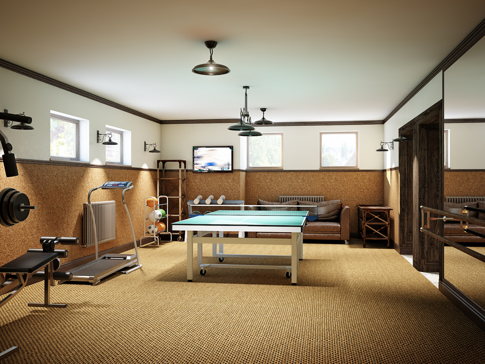 A remodeled basement that has been turned into a home gym. A ping pong table lies at the center of a room, surrounded by exercise machines and workout equipment
