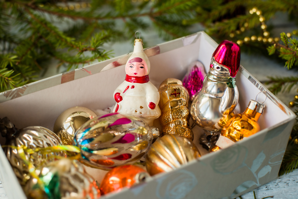 A white box filled with old Christmas ornaments. You can see the green branches of a Christmas tree in the background.
