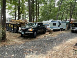 A pickup truck with a camper attached to it begins to drive through a gravel road in a forest.