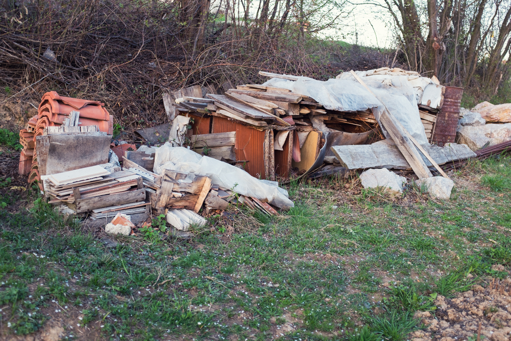 A heap of junk is seen on a backyard lawn. Among the pile, you can make out metal tiles and old pieces of wood.
