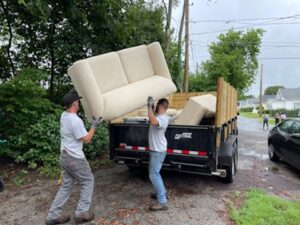 Trash bandits workers work together to toss an old couch into the bed of a pickup truck