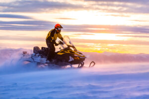 A man riding a snowmobile at sunset
