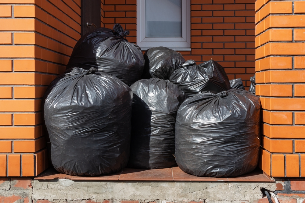 A pile of large black bags of garbage near the house.